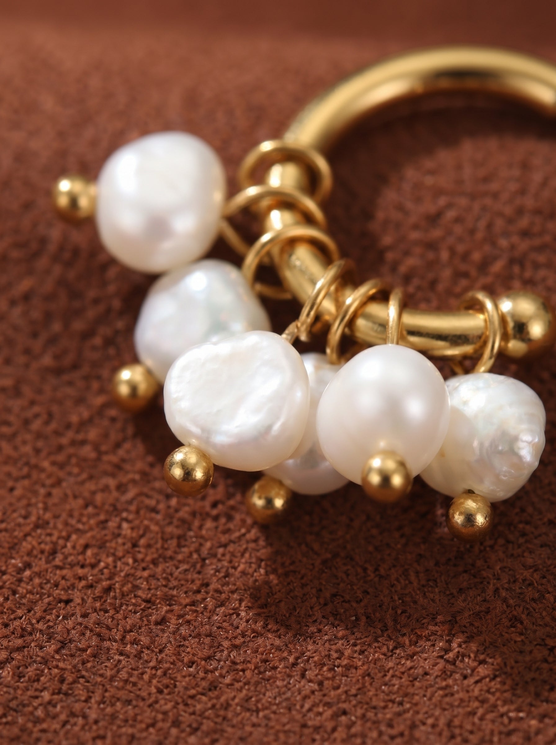 Close-up of gold hoop drop earrings featuring a cluster of irregular white freshwater seed pearls and small gold beads. @pearl