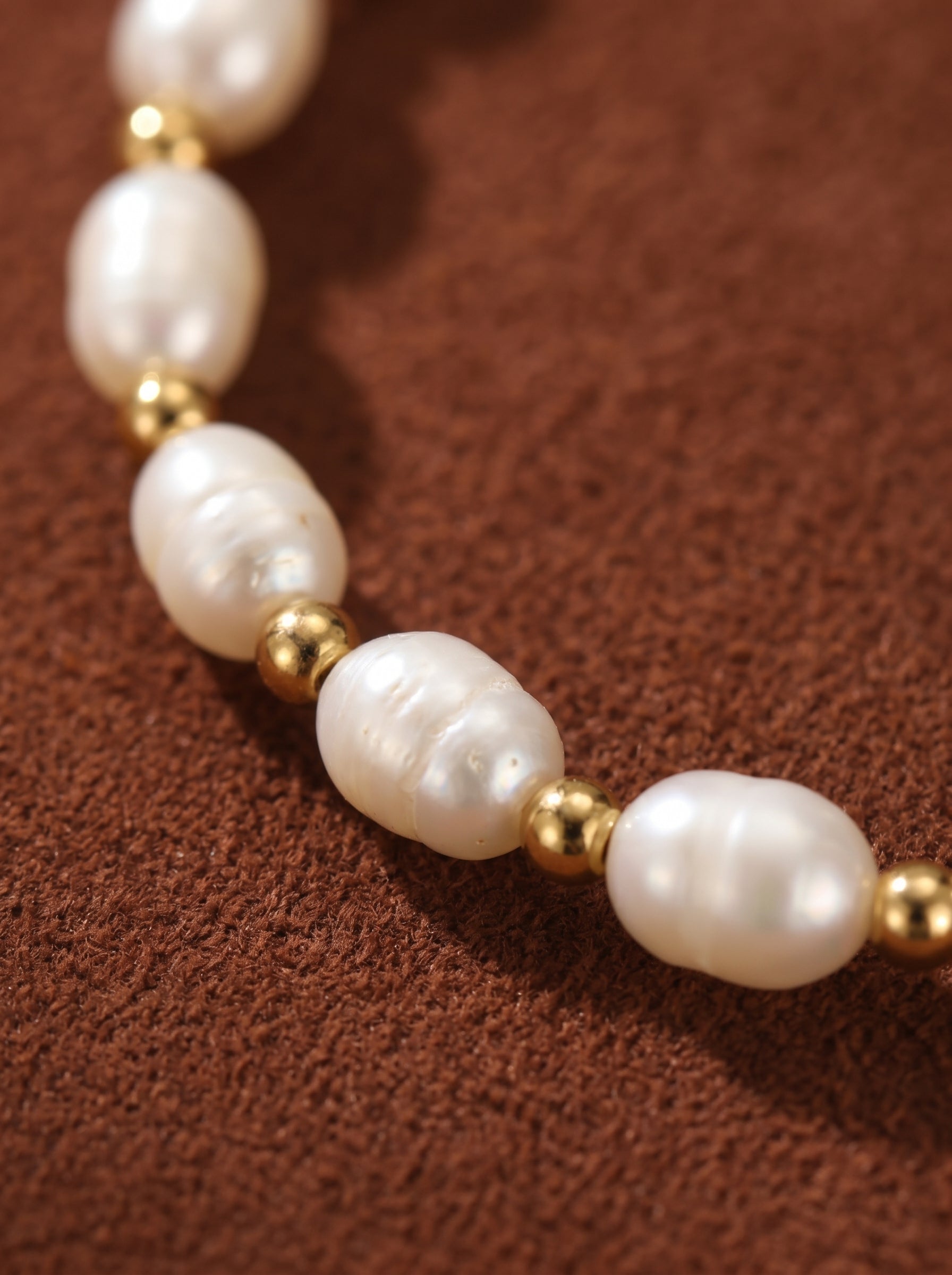 Delicate freshwater pearl beaded chain bracelet with gold-toned beads on a brown textured background.@pearl