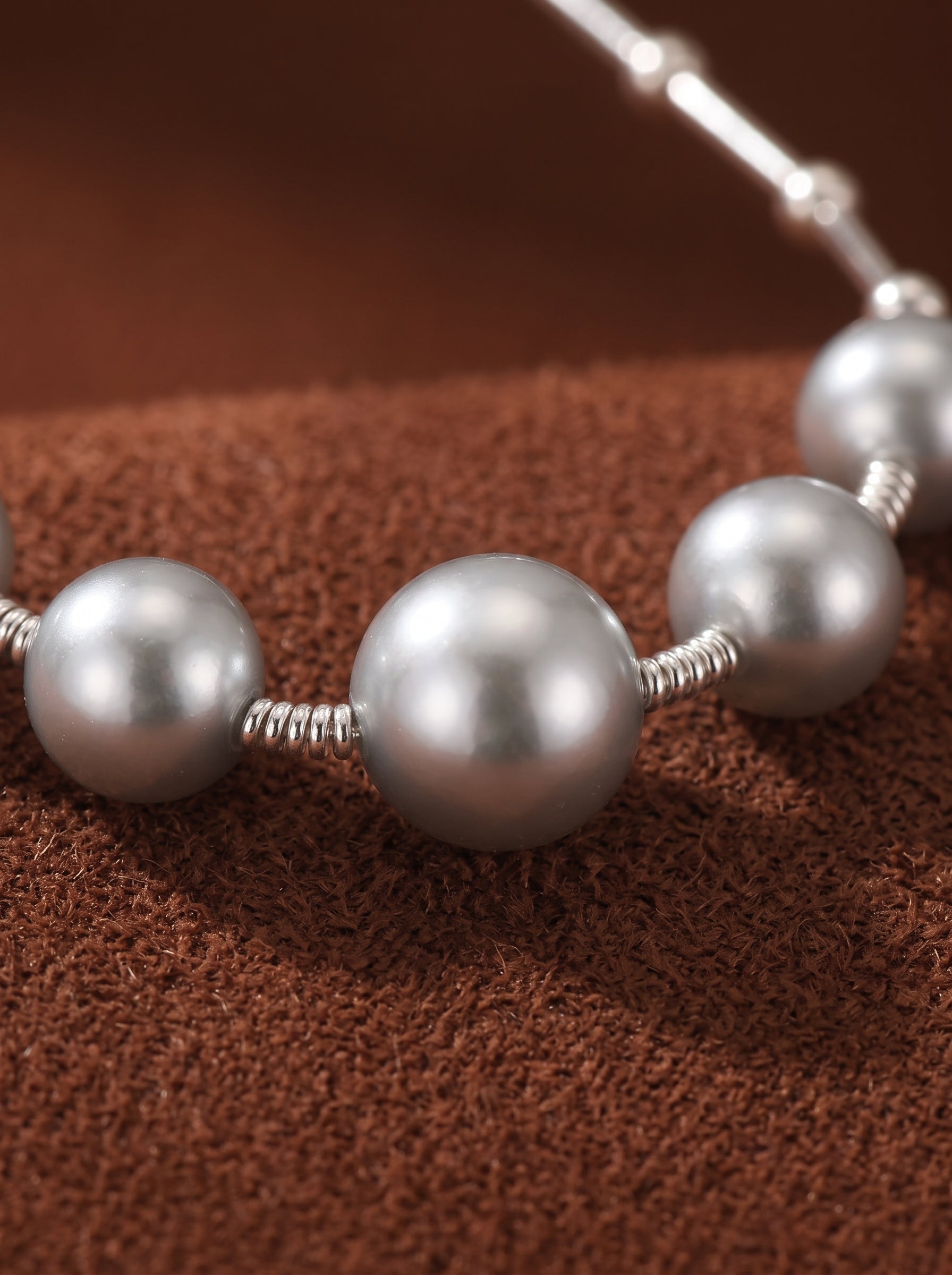 Close-up of a delicate necklace featuring several lustrous, silver-toned Akoya pearls spaced along a fine chain, with wire wrapping visible around each pearl. The necklace rests on a textured brown surface. @pearl