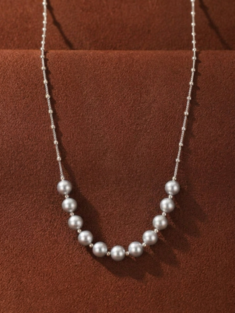Scatter Akoya Pearl Floating Necklace with a delicate silver chain and spaced lustrous grey pearls against a textured brown background.