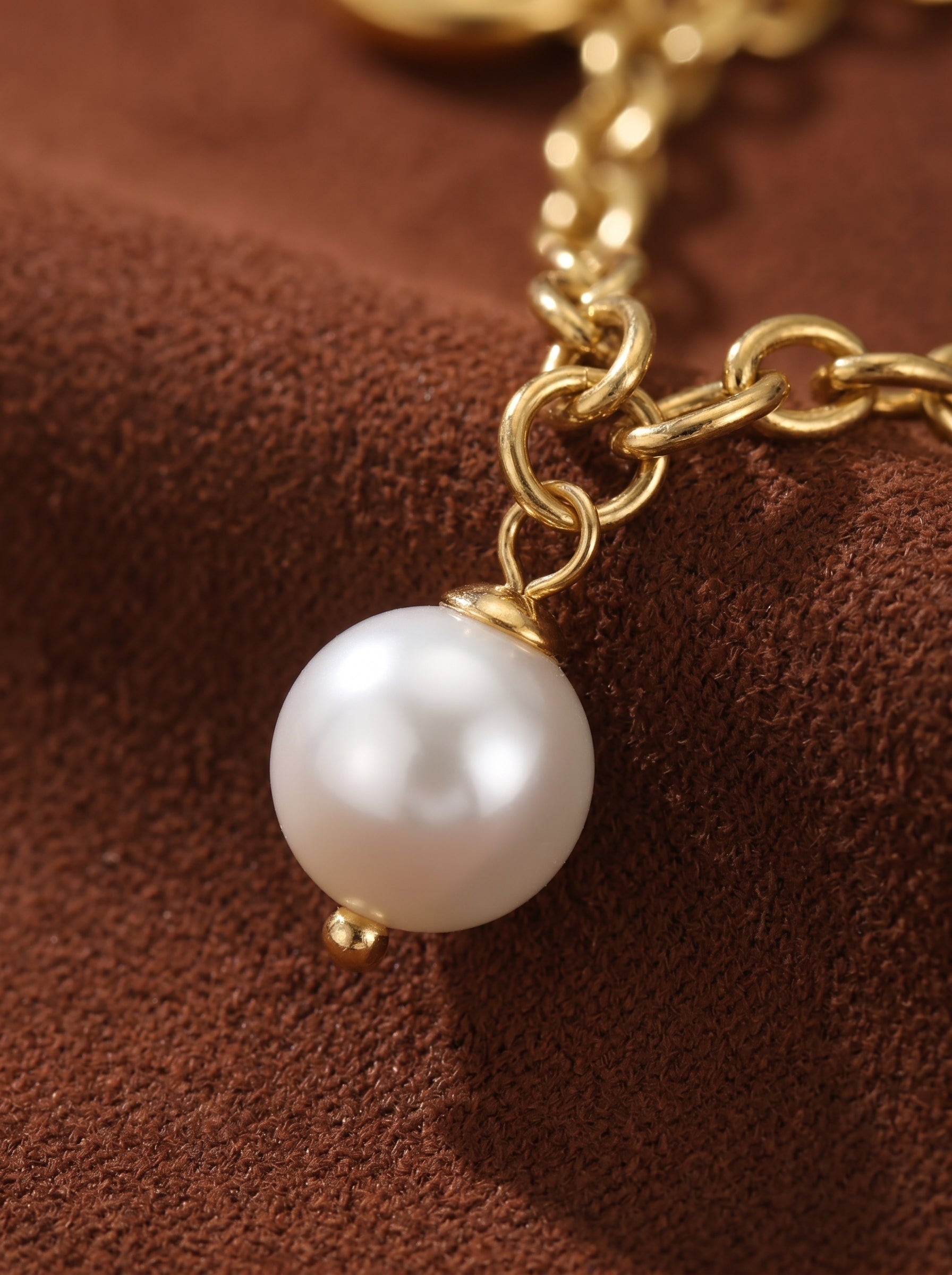 Close-up of a gold chain bracelet with a single lustrous freshwater pearl charm.@pearl