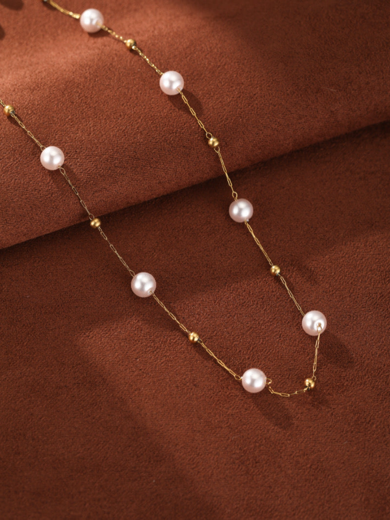 Un délicat collier à chaîne ton or présentant de petites perles roses d'eau douce et de minuscules perles dorées, disposé sur fond texturé marron.