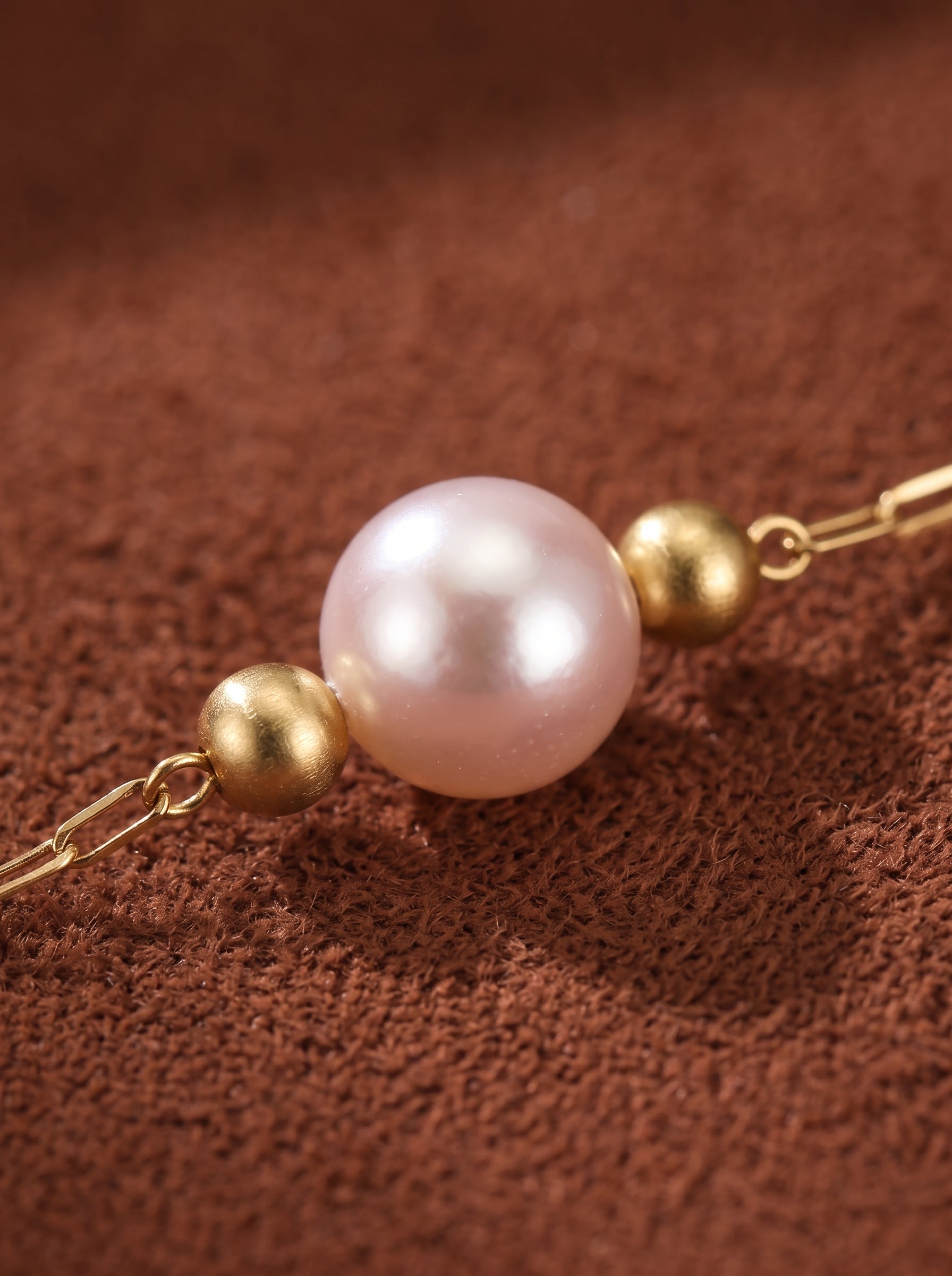 Gros plan du collier Seraph présentant une seule perle rose d'eau douce centrée entre deux petites perles dorées sur une délicate chaîne dorée. @pearl