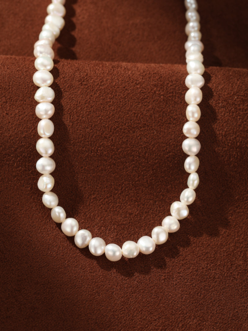 A close-up of the Serene Strand Freshwater Pearl Choker Necklace, featuring a strand of lustrous 6mm white button pearls resting on a brown textured background.@pearl