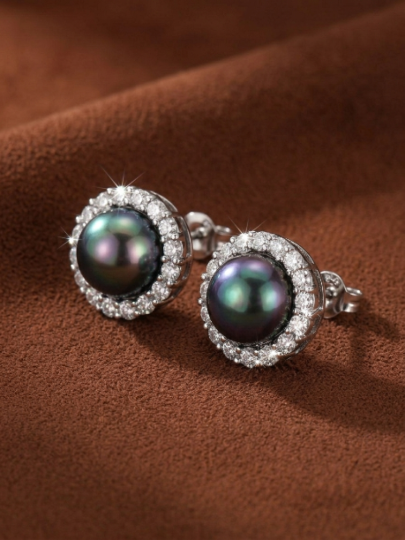 Close-up of two Shadowlight Tahitian pearl halo stud earrings with iridescent dark pearls surrounded by sparkling accent stones, set against a textured brown background.