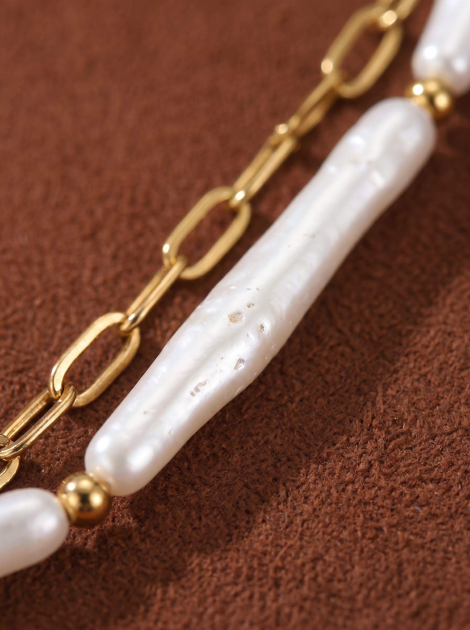 Close-up of a gold-tone oval link chain layered with elongated white imitation pearls and gold beads from the Shoreline necklace.@pearl