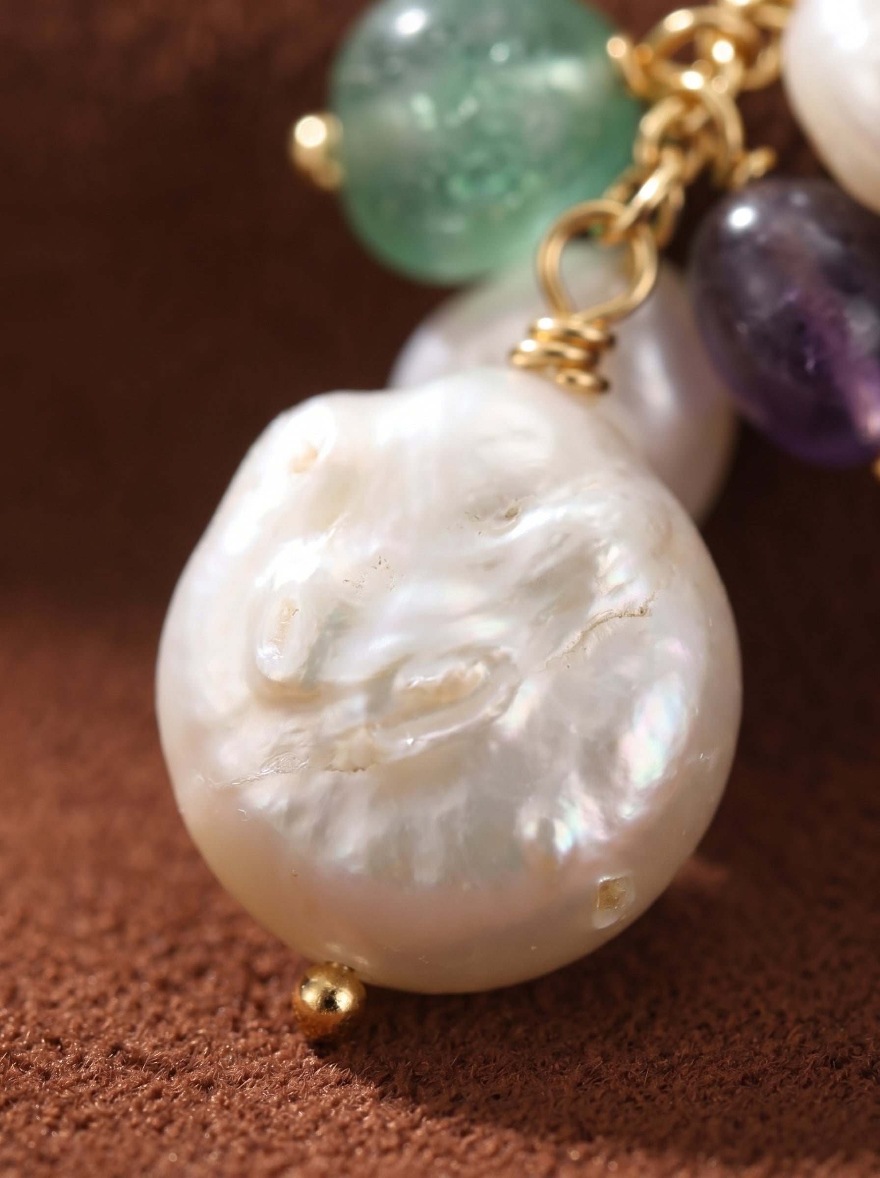 Close-up of Solana Freshwater Pearl Flower Dangle Earrings showcasing a large, irregular white baroque pearl with green and purple accent beads and gold wire details. @pearl