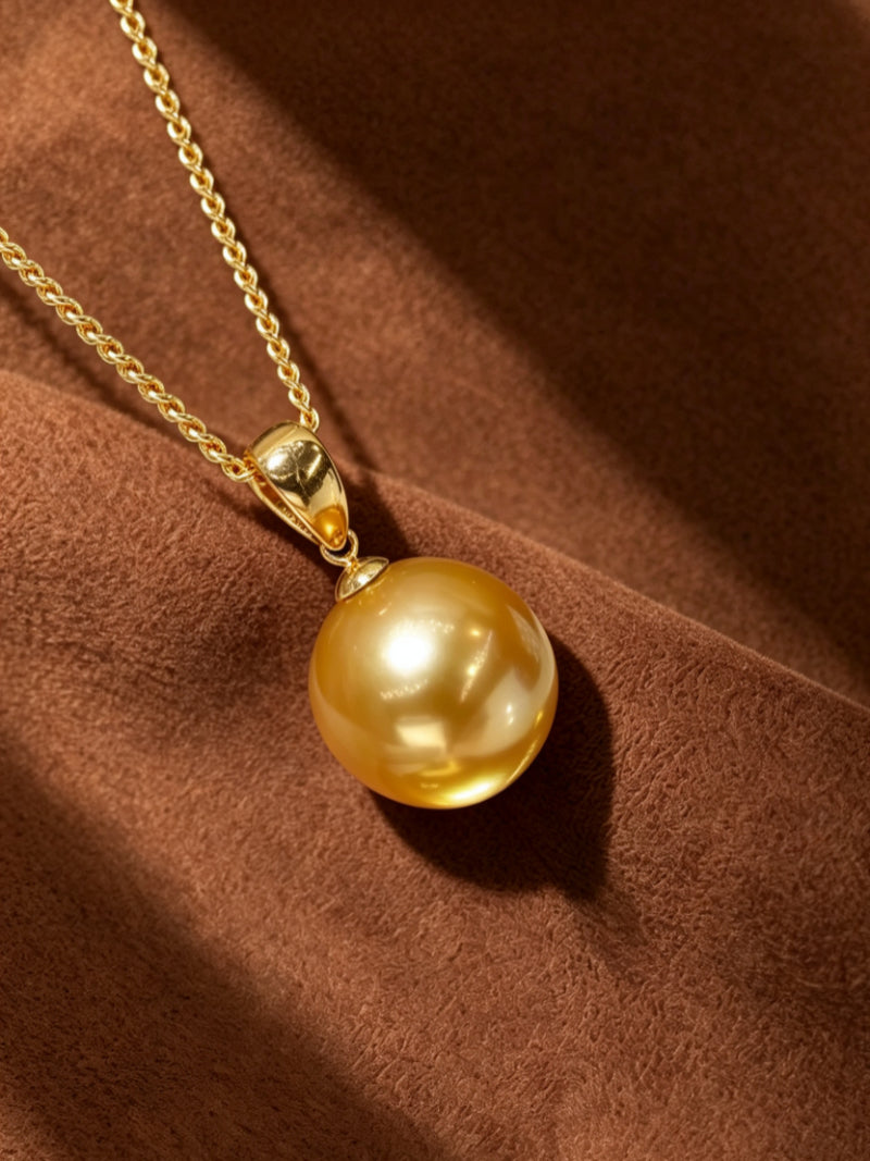 Solar Kiss necklace featuring a large, round golden freshwater pearl pendant suspended on a delicate gold-tone chain against a textured brown background.