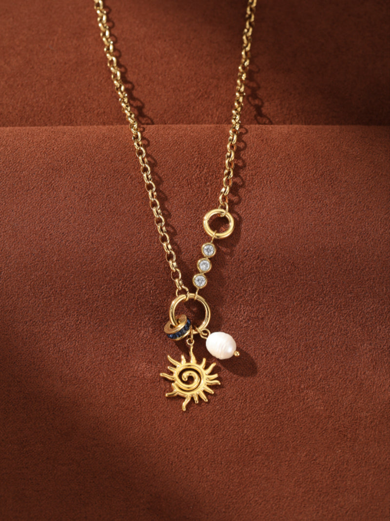 Gold-tone chain necklace with a sun pendant, a white freshwater pearl, and blue accent beads, adorned with sparkling stones and delicate details. @pearl