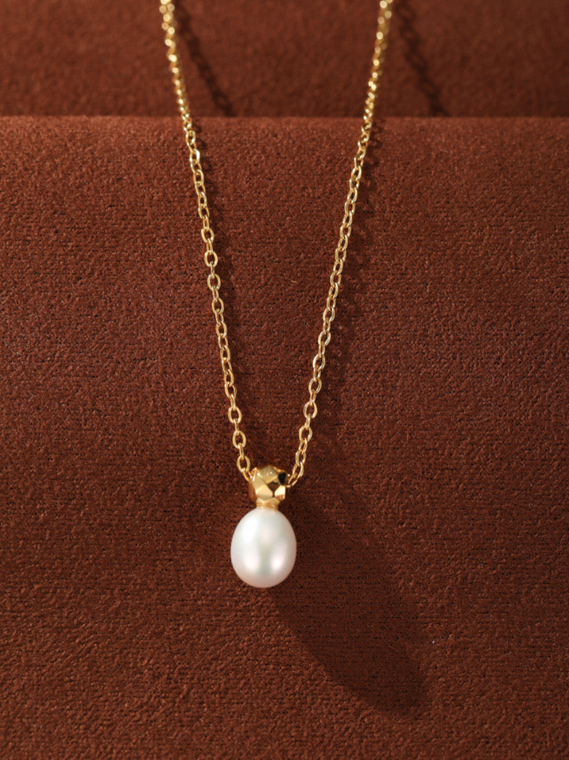 Un délicat collier à chaîne ton or présentant une seule et lustrée perle blanche pendante d'eau douce. La perle est maintenue par un capuchon géométrique facetté ton or, créant un design moderne et élégant.