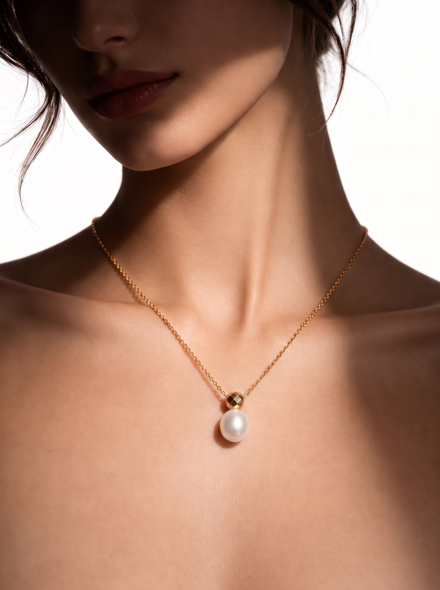 Gros plan d'une femme portant le collier pendentif goutte solitaire Solitaire en perle d'eau douce, présentant une seule et lustrée perle blanche suspendue à une délicate chaîne ton or avec un capuchon doré facetté. @model
