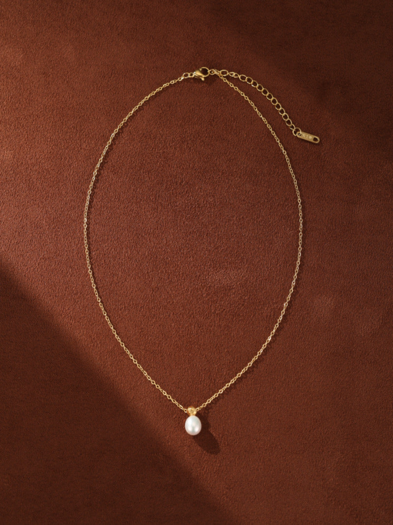 Un délicat collier à chaîne ton or présentant une seule et lustrée perle graine blanche d'eau douce suspendue à un capuchon facetté ton or.
