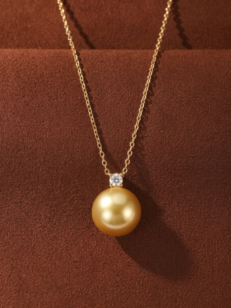 A single, luminous 9 mm round golden South Sea pearl pendant necklace with a brilliant diamond accent on a delicate gold chain.