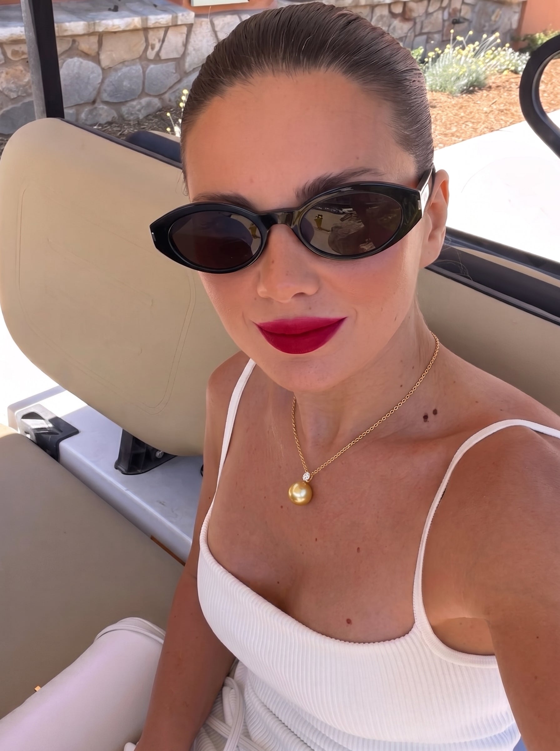 A woman wearing a white top and black sunglasses, showcasing a Sovereign South Sea pearl pendant necklace with a diamond accent, while sitting in a golf cart. @lifestyle