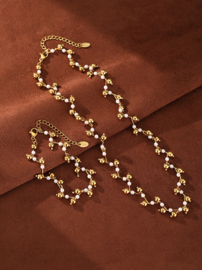 Stardust Mother of Pearl Beaded Bracelet featuring small white pearls and gold-toned spheres with an organic, branch-like design on a brown background.