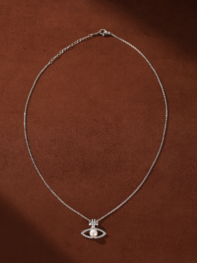 Stellar Gaze necklace with an eye-shaped pendant featuring a 6 mm button freshwater pearl, sparkling accents, and a small cross detail, on a delicate silver chain.@pearl
