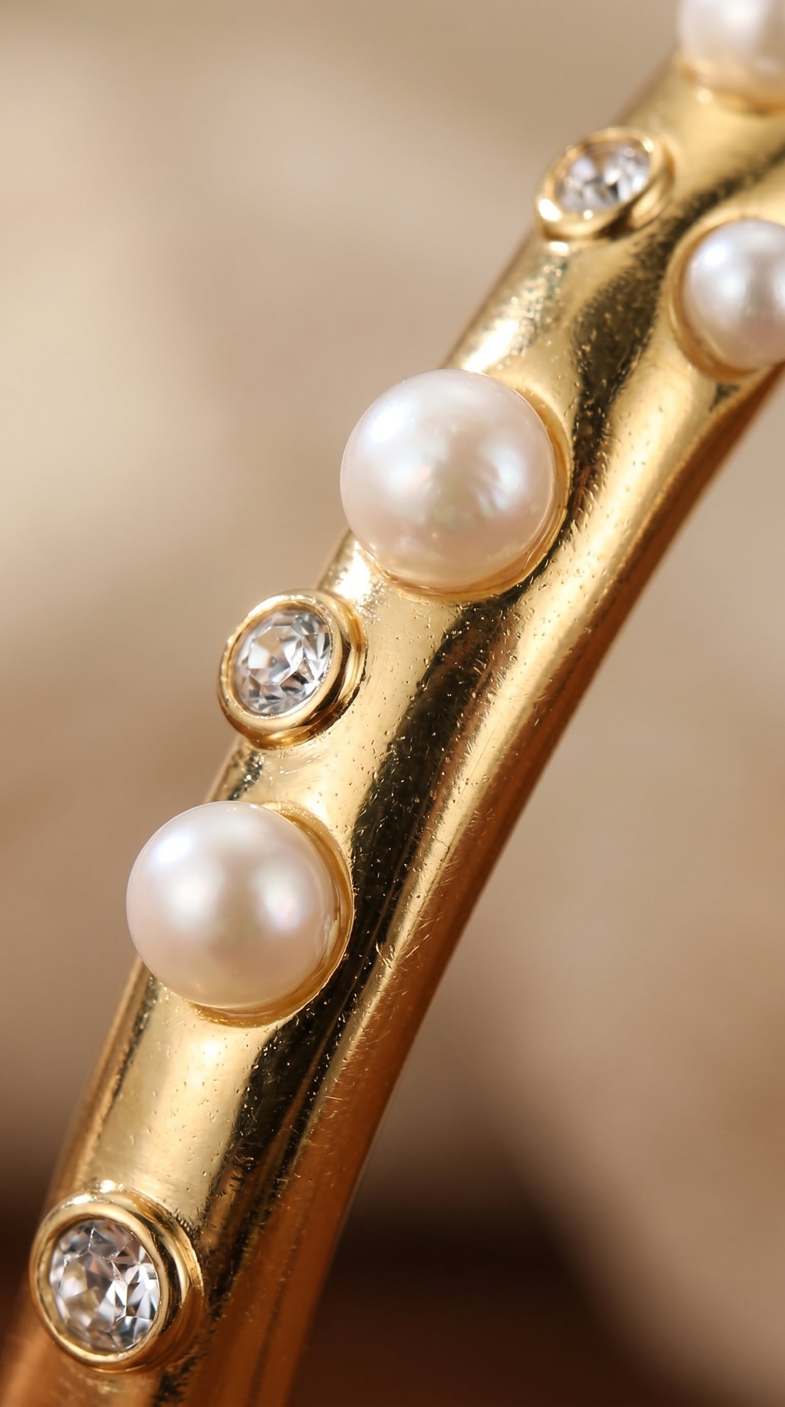 Close-up of a gold cuff bracelet featuring round imitation pearls and sparkling accent stones. @pearl