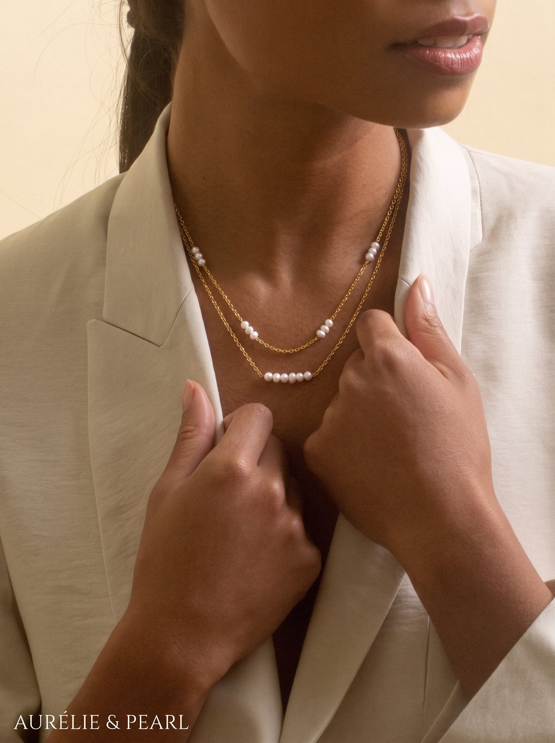 A woman wearing a beige blazer, showcasing the Stellaris layered necklace with delicate freshwater pearls spaced along thin gold chains. @model