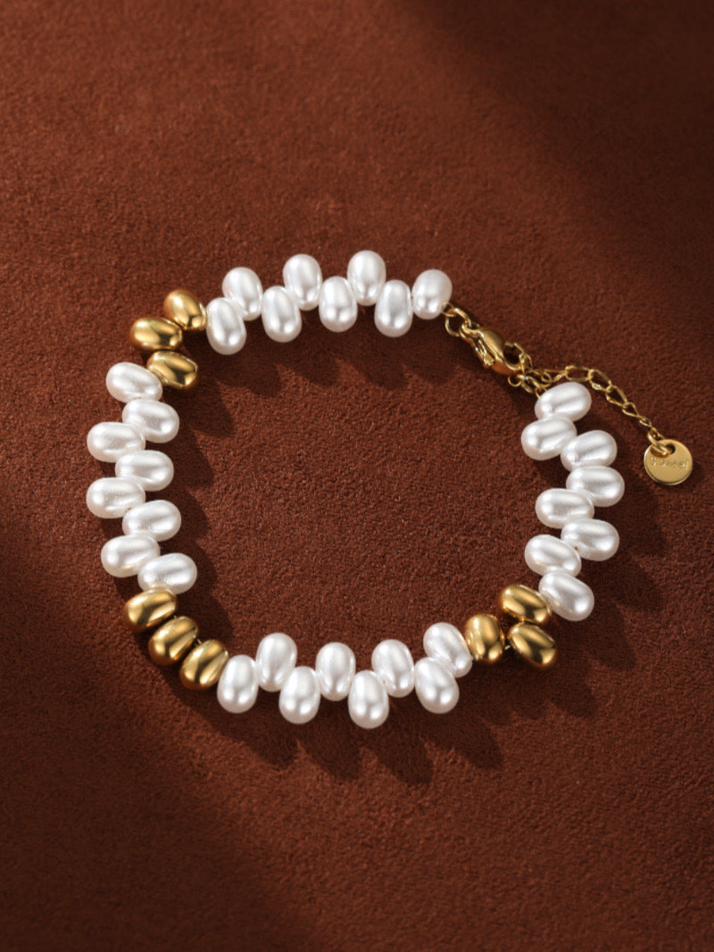 A Sylvan bracelet featuring lustrous white freshwater seed pearls interspersed with polished gold-toned beads on a brown background.