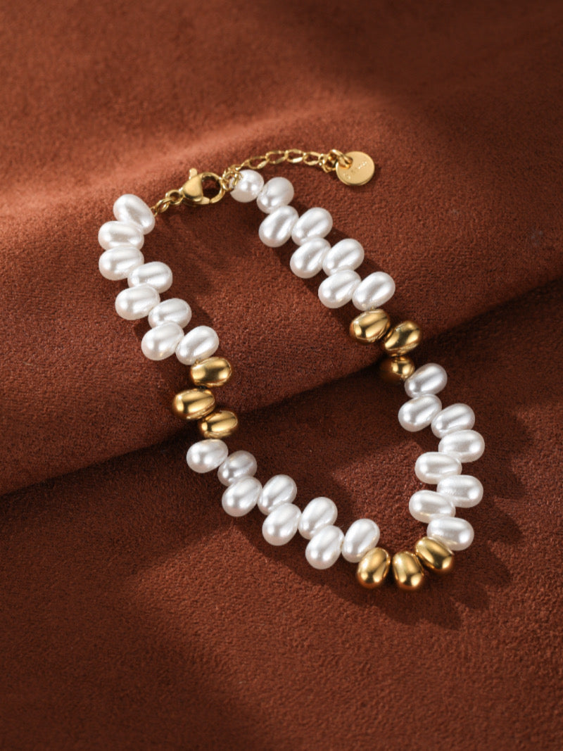 Sylvan bracelet featuring white freshwater seed pearls and polished gold-toned beads on a brown textured background.