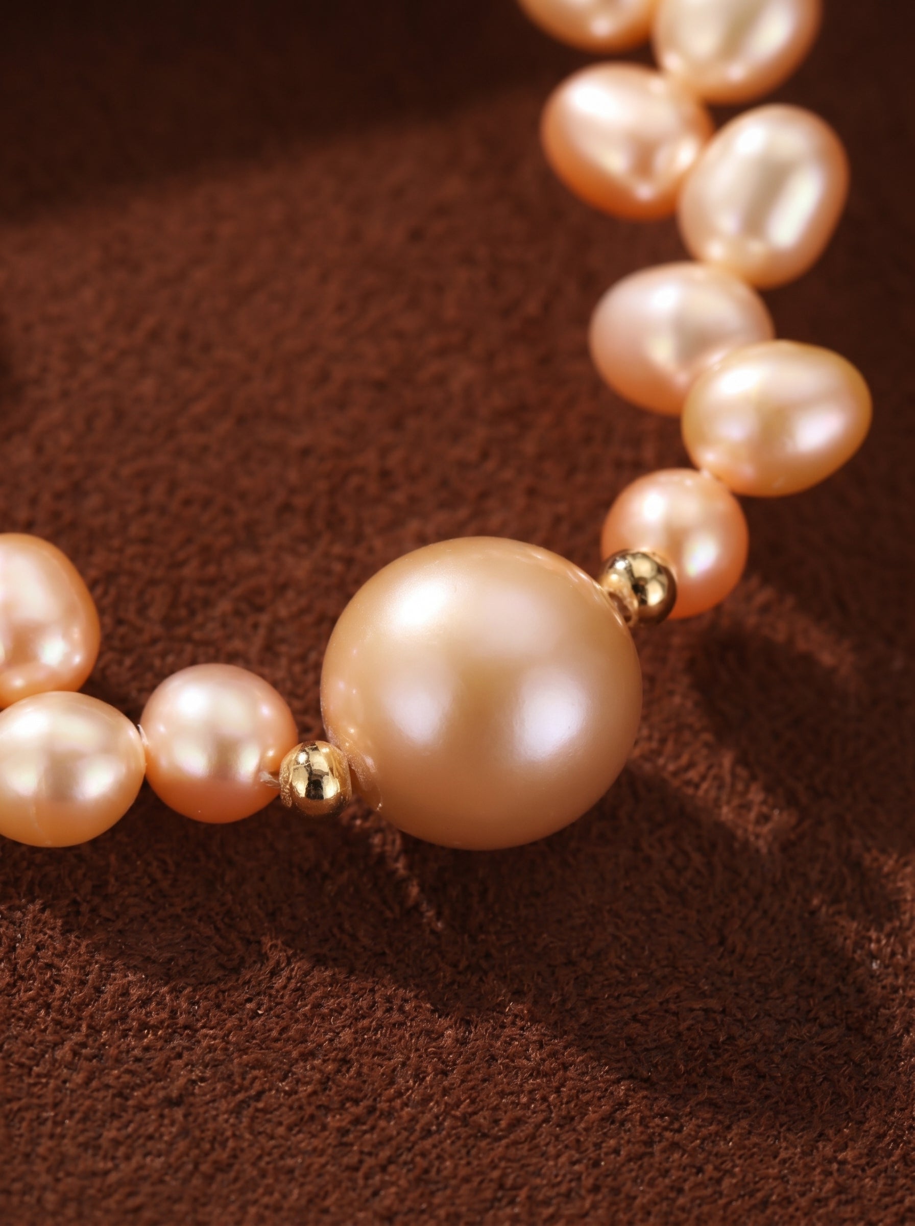 Tendril choker necklace featuring a strand of delicate pink freshwater pearls of varying sizes, with a single larger round pearl as a focal point, separated by small gold beads, on a textured brown background.
