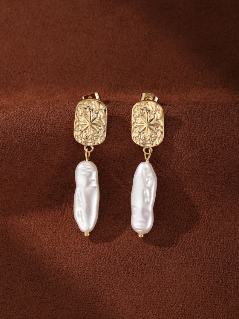 Boucles d'oreilles goutte en perle d'eau douce Terra présentant des puces rectangulaires texturées ton or au design en éclat de soleil et des gouttes de perle baroque blanche irrégulières.