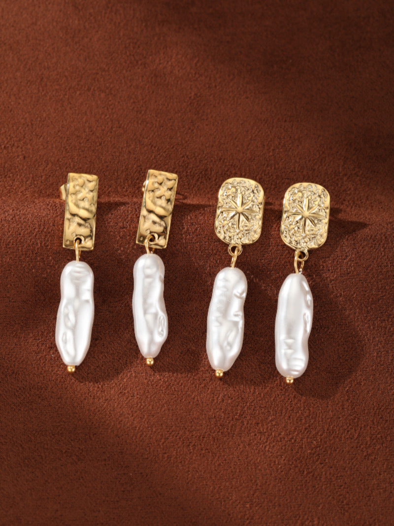 Boucles d'oreilles goutte en perle d'eau douce Terra avec des puces rectangulaires martelées ton or et des gouttes de perle baroque blanche irrégulières sur fond marron.
