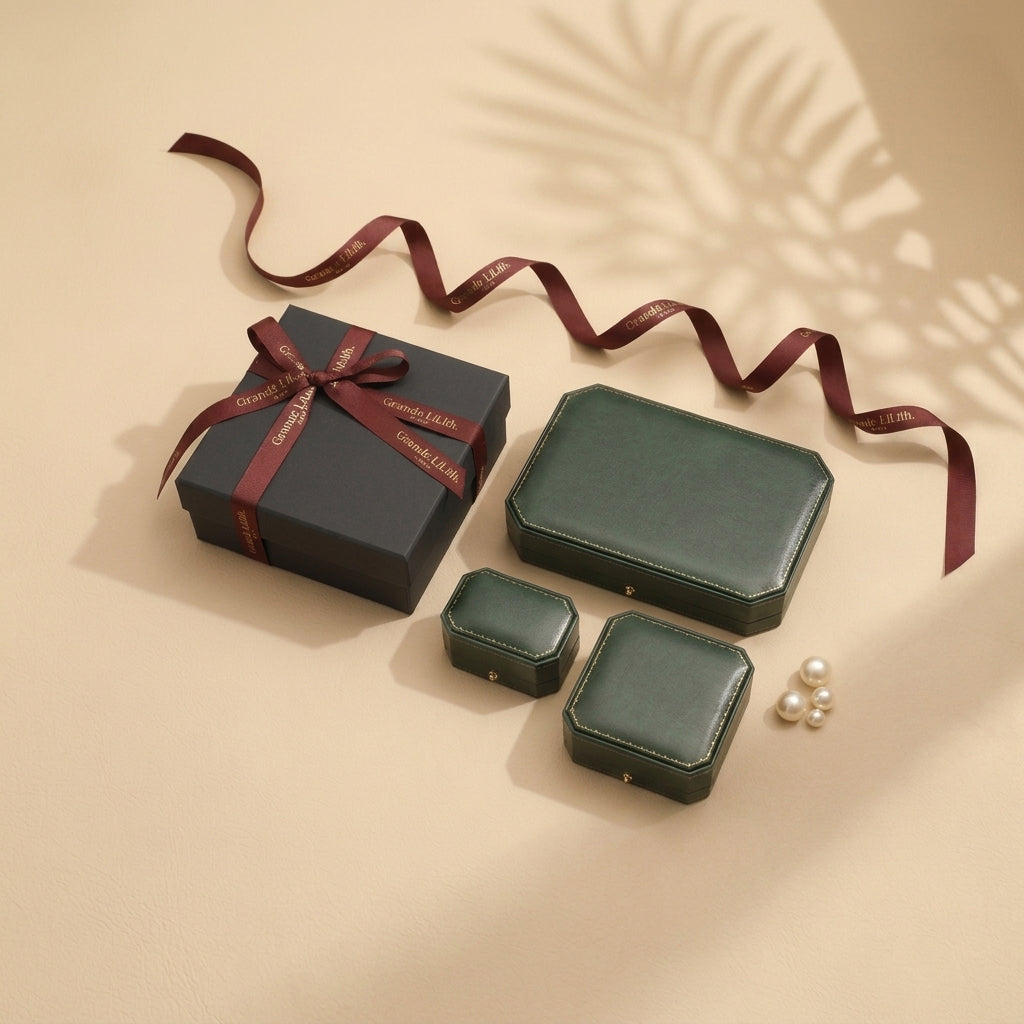 A set of vintage-style green jewelry boxes with push-button clasps, alongside a dark gift box tied with a burgundy ribbon. A few pearls are scattered nearby. The arrangement is set against a neutral background with soft shadows.