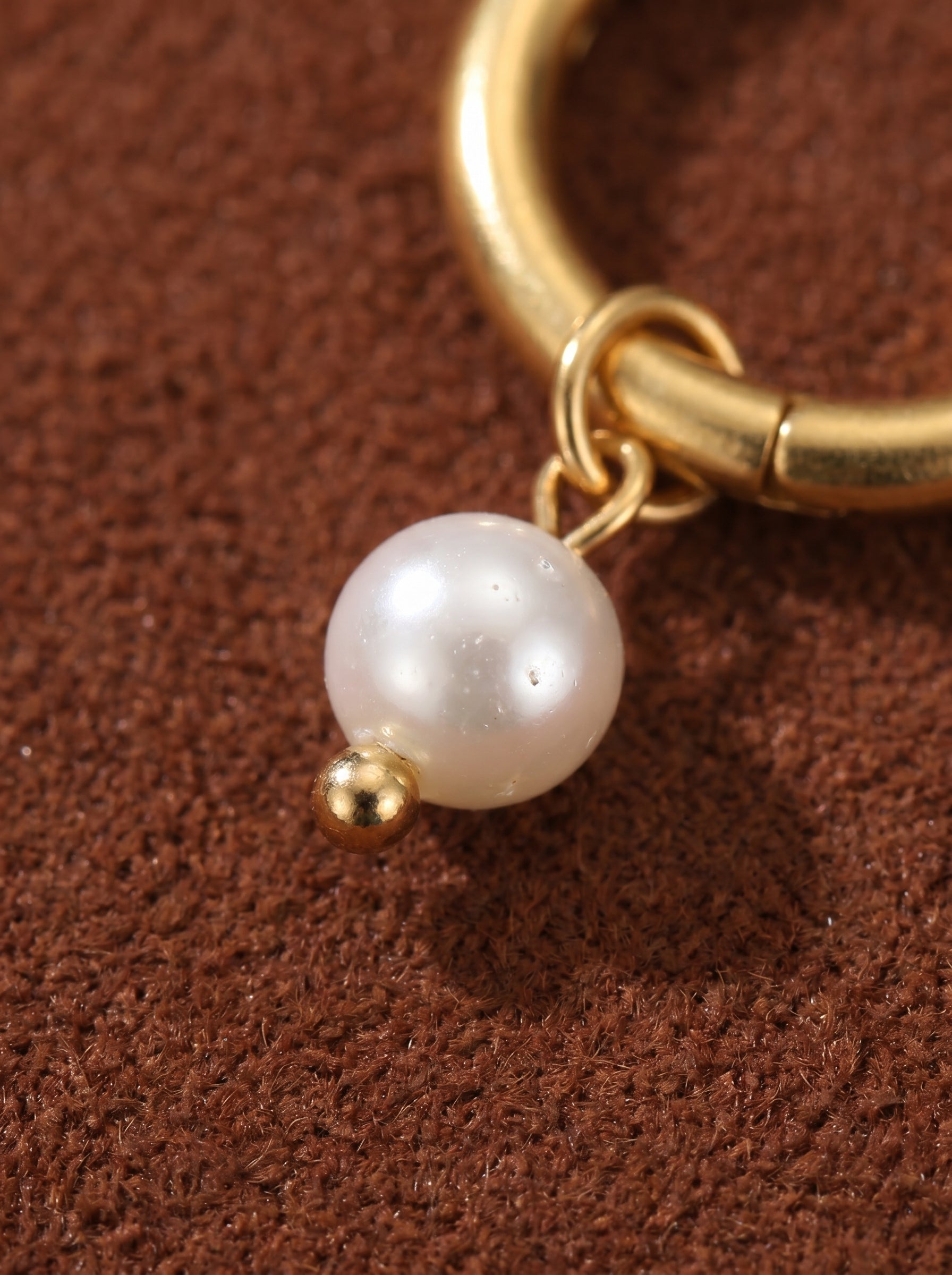 Close-up of a gold hoop earring with a delicate freshwater pearl charm and a small gold bead accent. @pearl