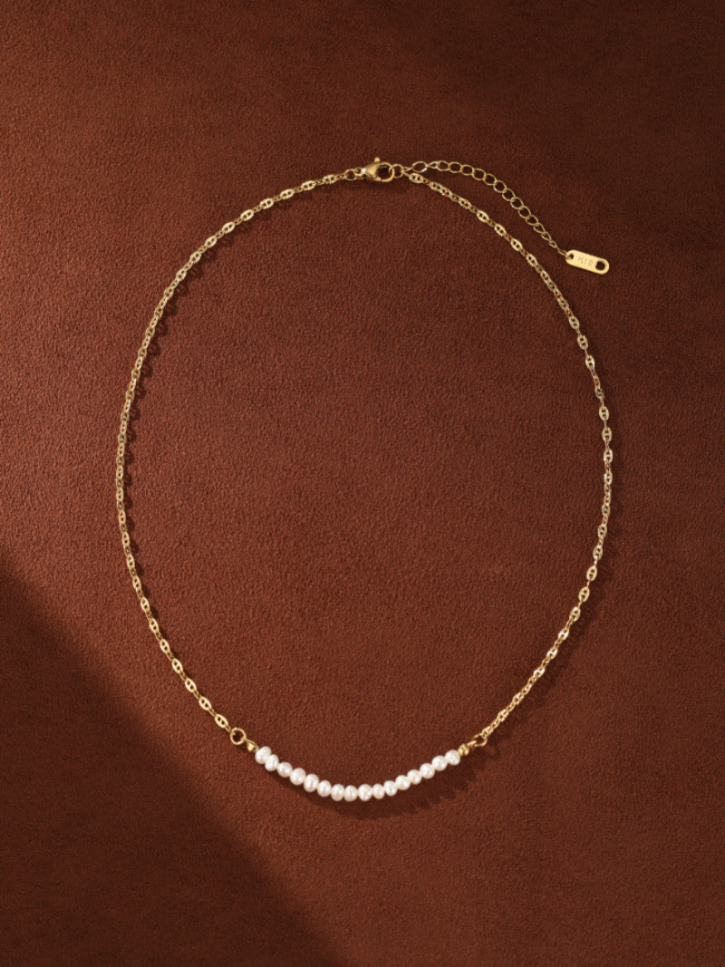 Un délicat collier à chaîne ton or avec un subtil arc de petites et lustrées perles blanches d'eau douce.