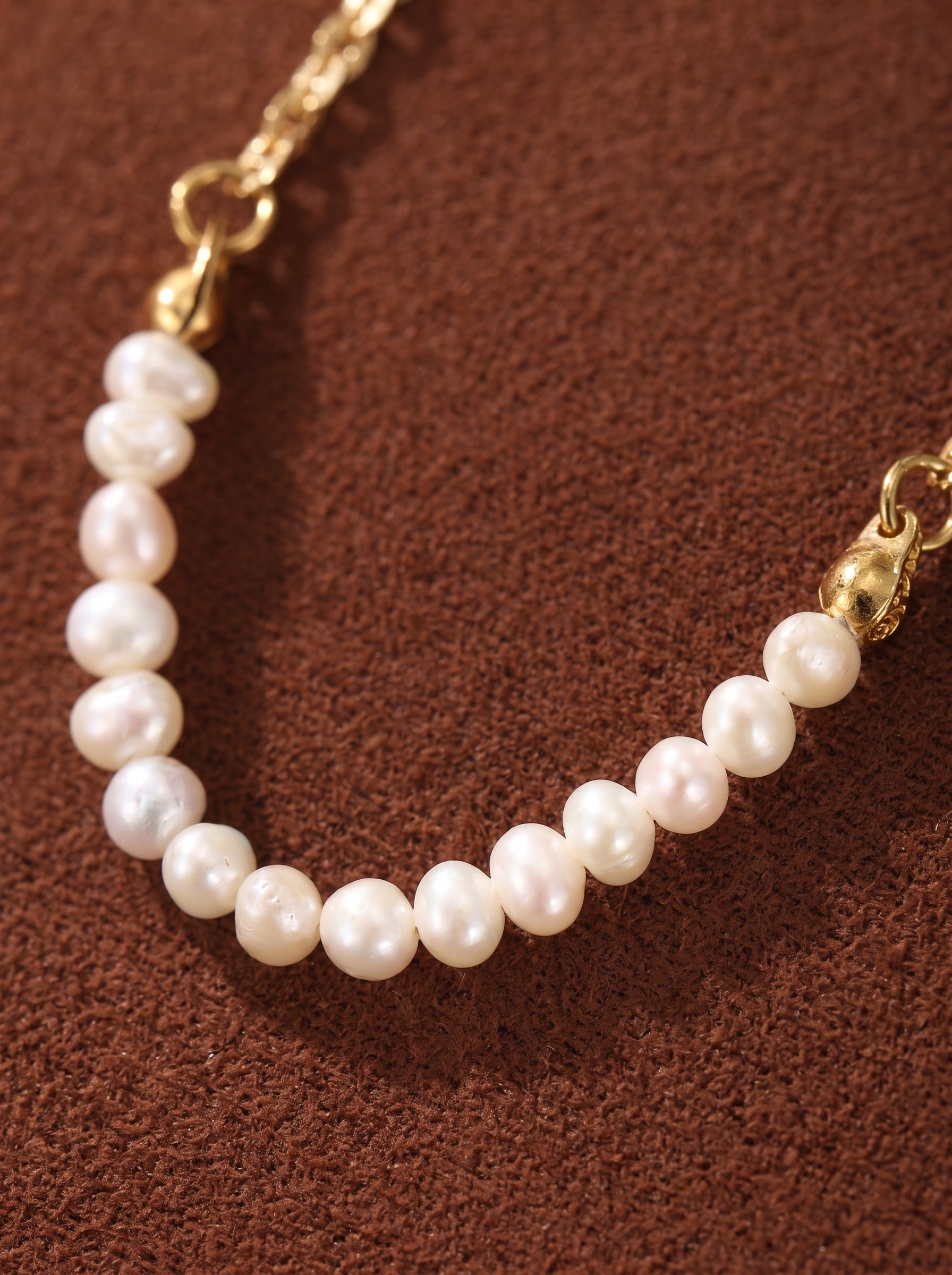 Gros plan d'un délicat collier à chaîne ton or présentant une rangée graduée de lustrées perles bouton blanches d'eau douce de 3 mm enfilées sur une fine chaîne dorée. @pearl