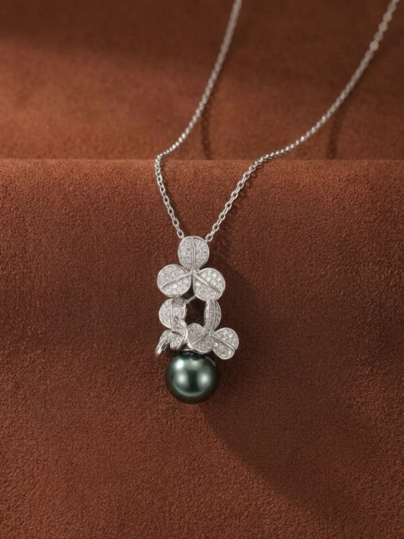 A close-up studio shot of the Unfold Tahitian Pearl Clover Pendant Necklace, featuring a sterling silver chain, a clover-shaped pendant encrusted with small diamonds, and a single, lustrous 14mm round Tahitian pearl in a deep black hue.
