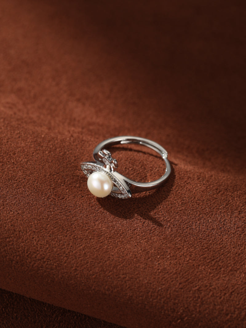 Silver-toned open cuff ring featuring a lustrous freshwater pearl at its center, surrounded by a pave-embellished cross design on a textured brown surface. @pearl