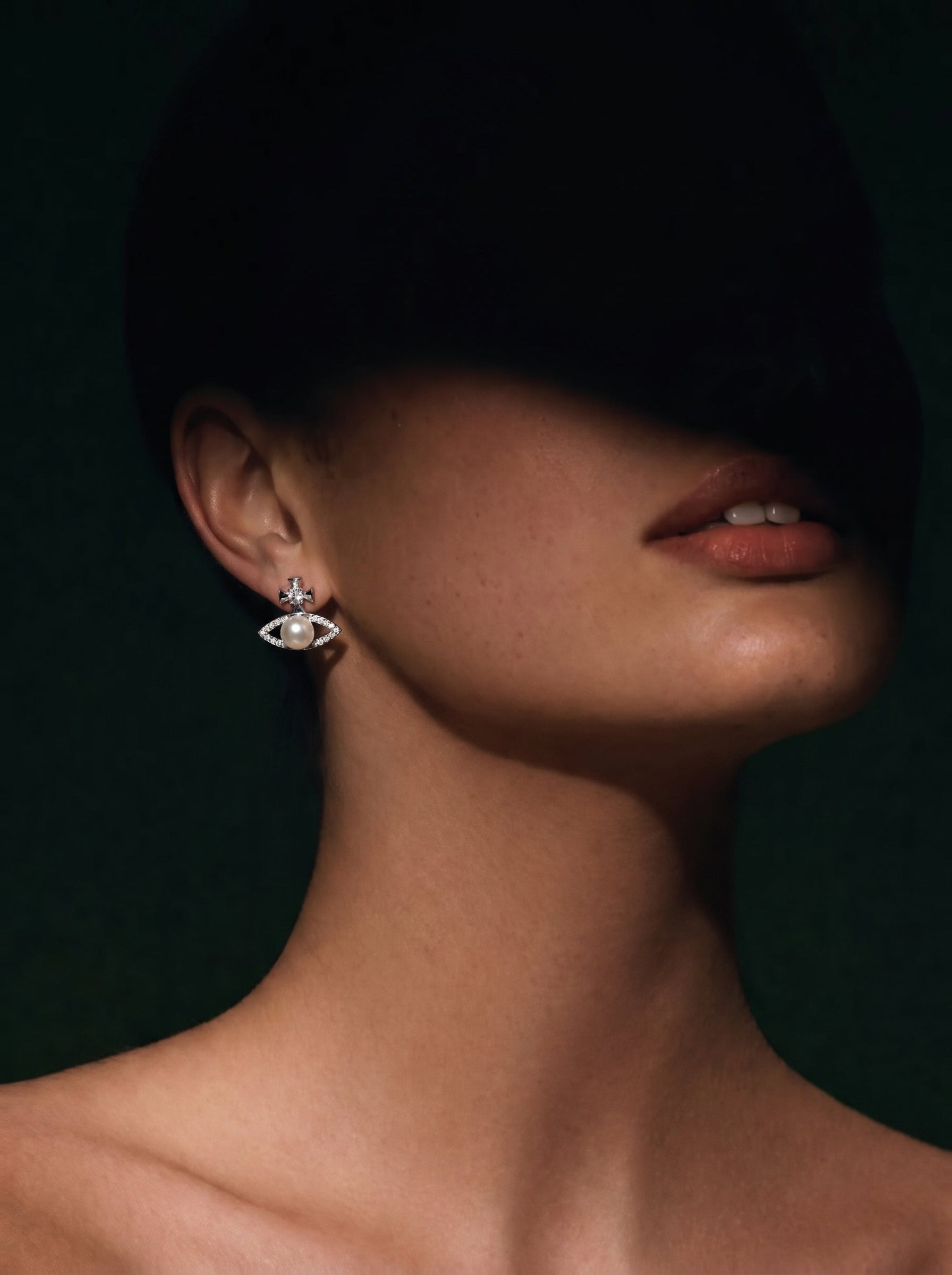 Close-up of a woman wearing Verity Freshwater Pearl Cross Stud Earrings featuring a white pearl set in a sparkling eye-shaped pavé frame with a cross motif. @model