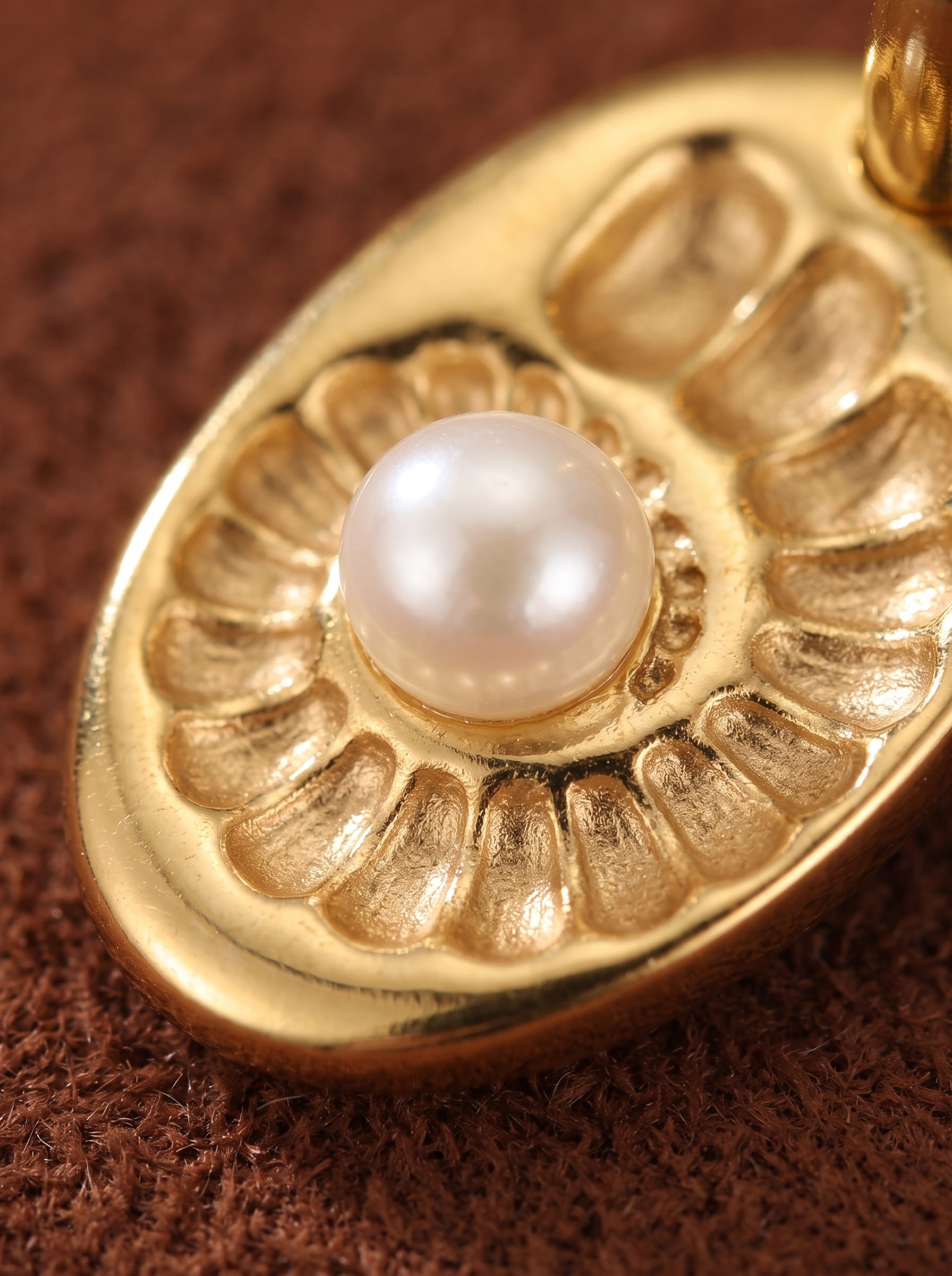 Close-up of a golden oval charm with a spiral embossed pattern, featuring a lustrous white freshwater button pearl at its center. The charm is part of the Vesica Freshwater Pearl Spiral Hoop Drop Earrings. @pearl
