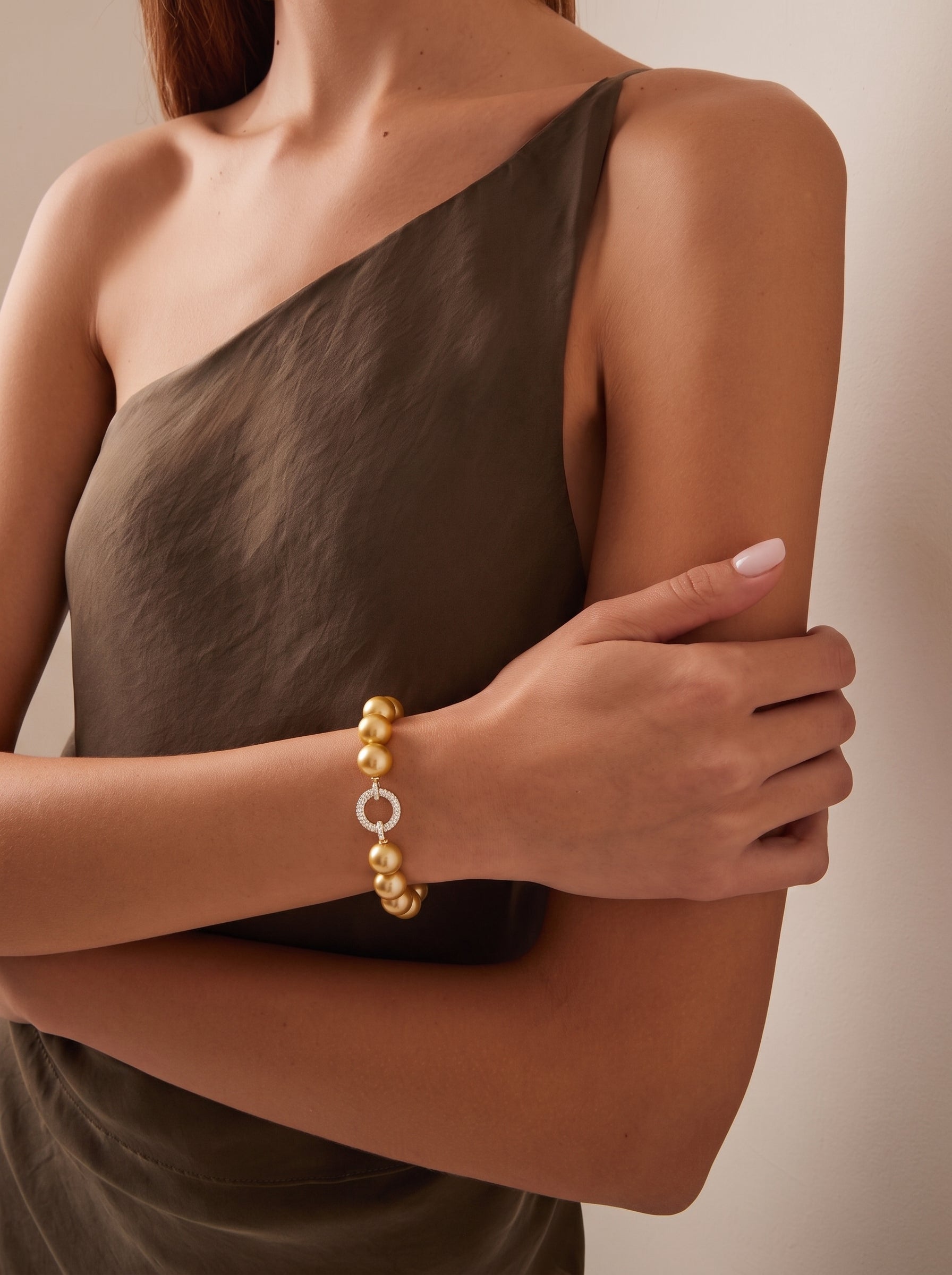 A woman wears a Vibrant Loop bracelet featuring golden freshwater pearls and a pavé-set circular clasp. The image is a lifestyle shot showcasing the bracelet on a model. @lifestyle