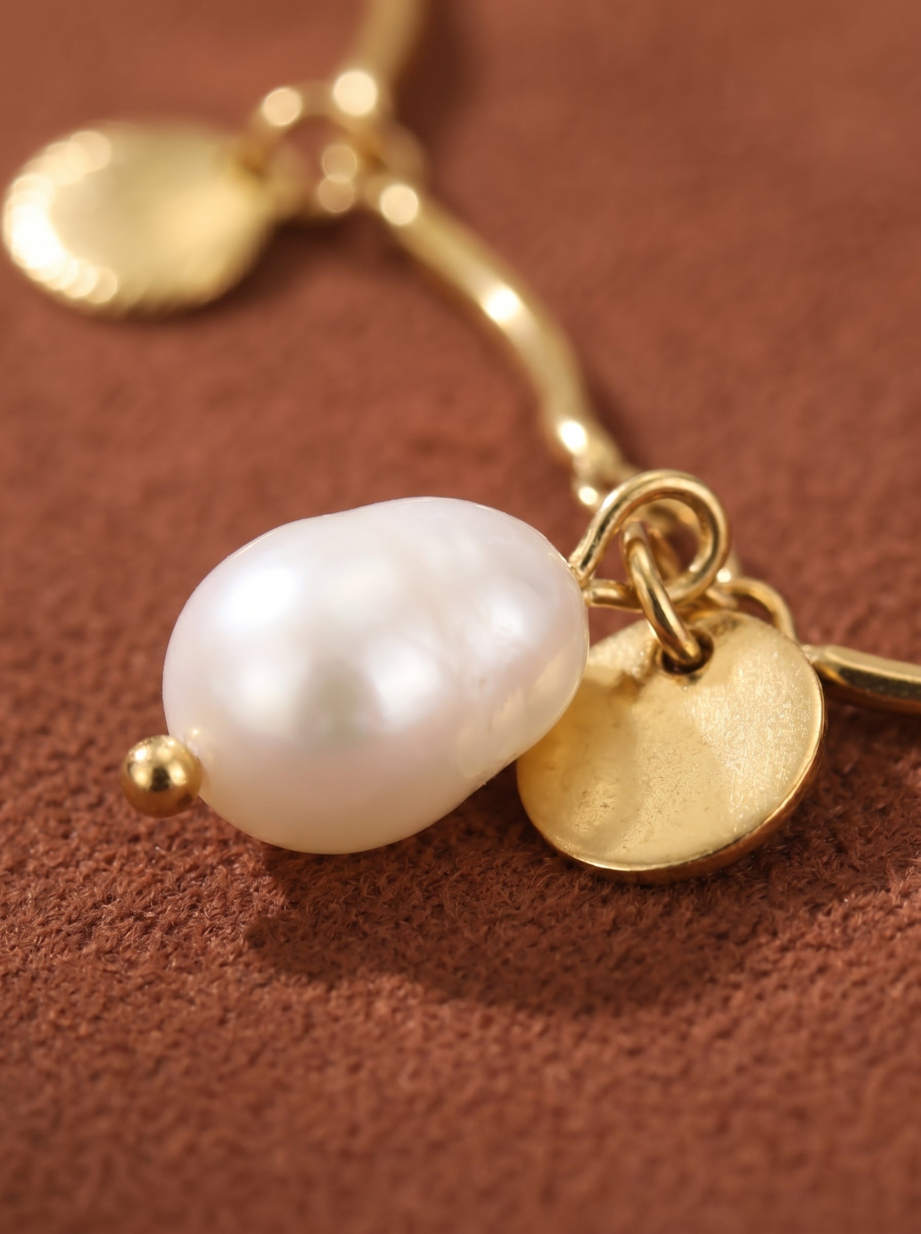 A close-up shot of a gold necklace featuring a wavy chain with a lustrous freshwater pearl and a small gold disc charm. @pearl