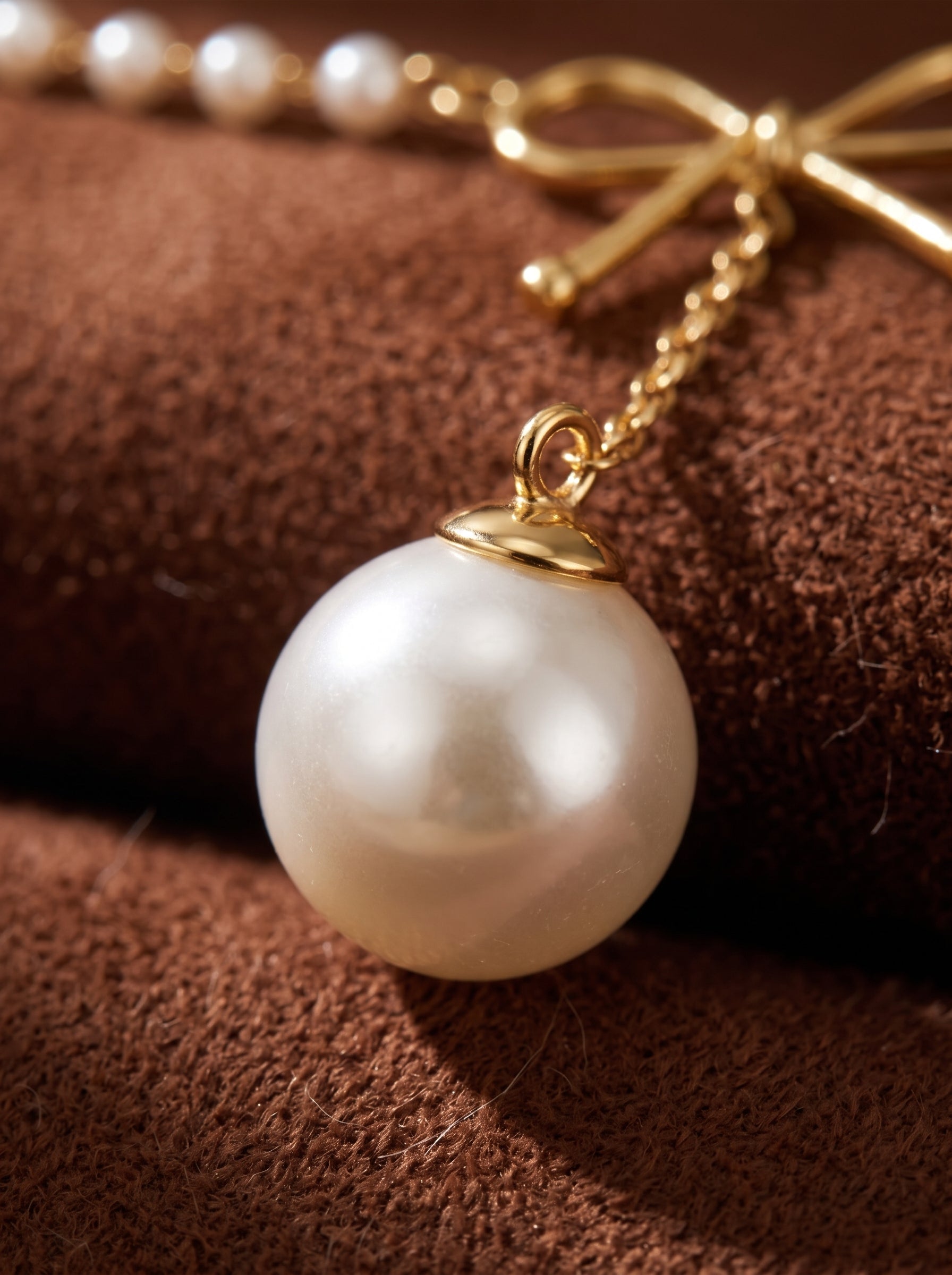 Close-up of a delicate gold-tone chain necklace featuring a large, lustrous imitation pearl drop pendant, with smaller beaded pearls and a subtle bow detail visible in the background. @pearl