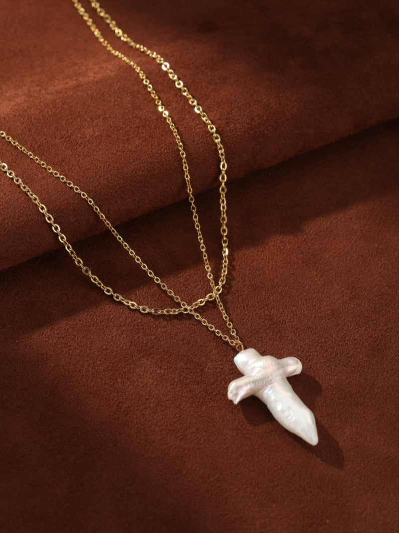 Aegis layered necklace featuring a gold-toned chain and a large white baroque freshwater pearl cross pendant.