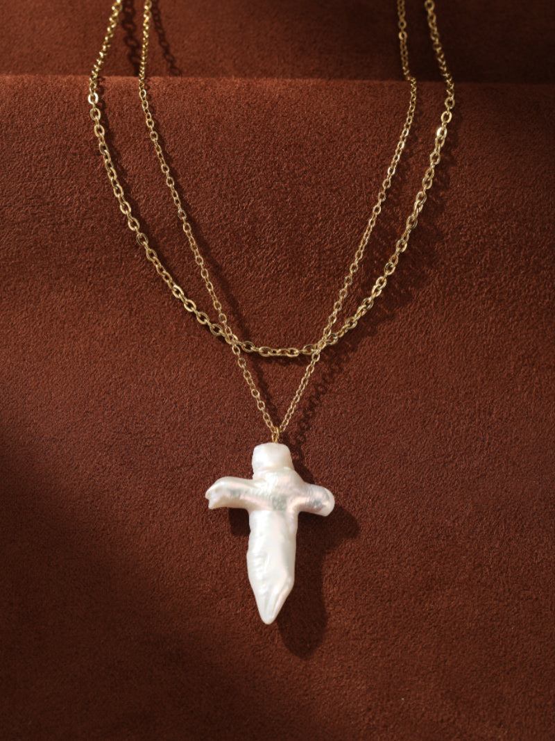 Aegis layered necklace featuring a large white freshwater baroque pearl cross pendant on a delicate gold-toned chain.@pearl