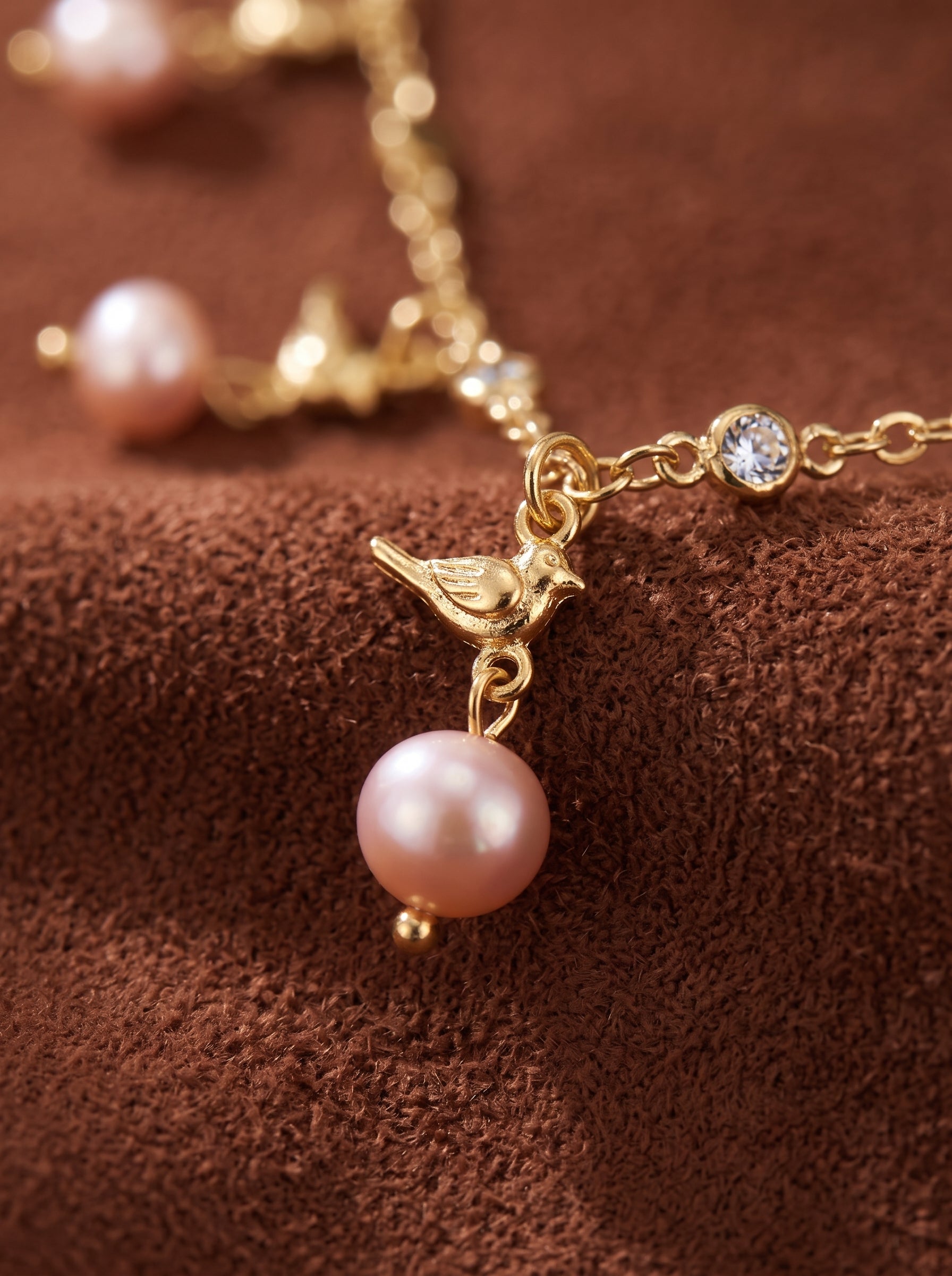 Un délicat collier à chaîne ton or présentant une charmante breloque oiseau et une perle d'eau douce, accentuée de petits cristaux transparents. @pearl