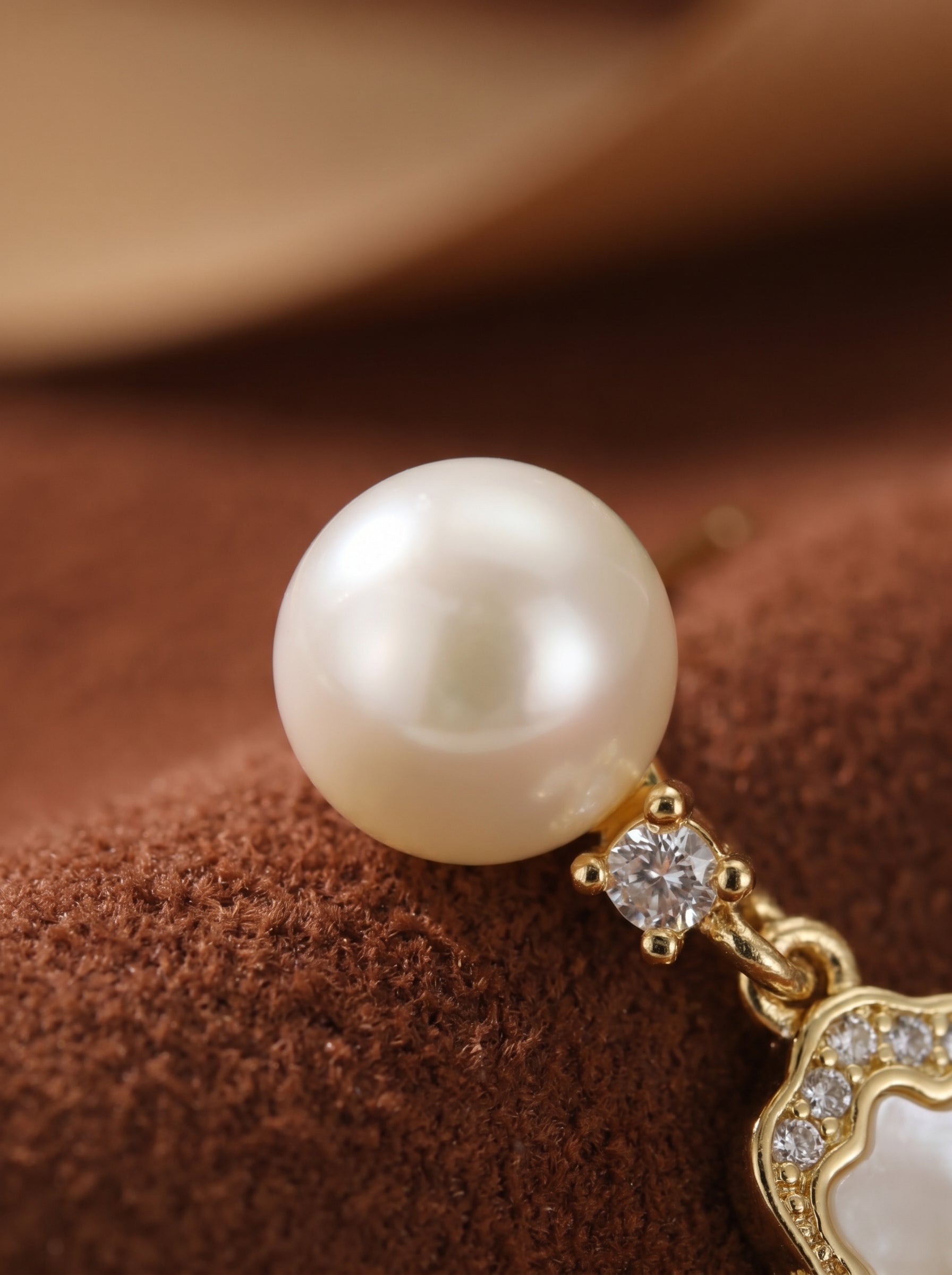 Close-up of Aethel gold-tone drop stud earrings featuring a lustrous white freshwater pearl suspended above a sparkling clear stone and a decorative motif. @pearl
