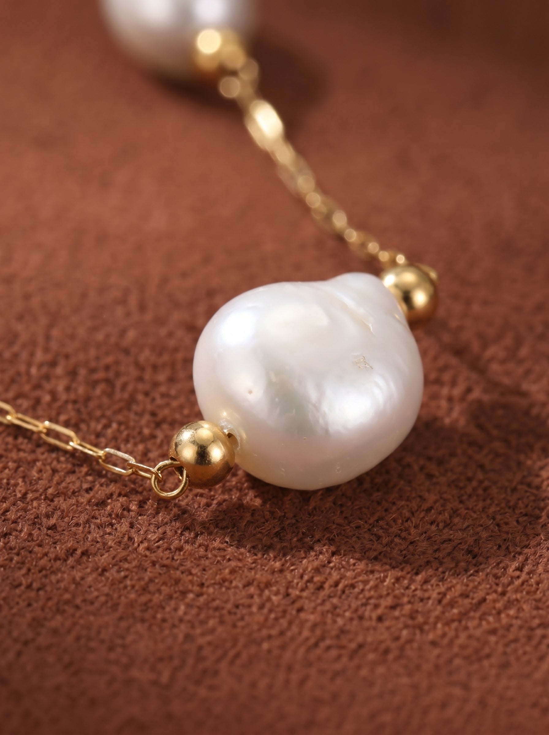 Close-up of a white freshwater pearl necklace with a delicate gold chain and small gold beads, on a textured brown background. Freshwater Pearl Floating Chain Necklace@pearl
