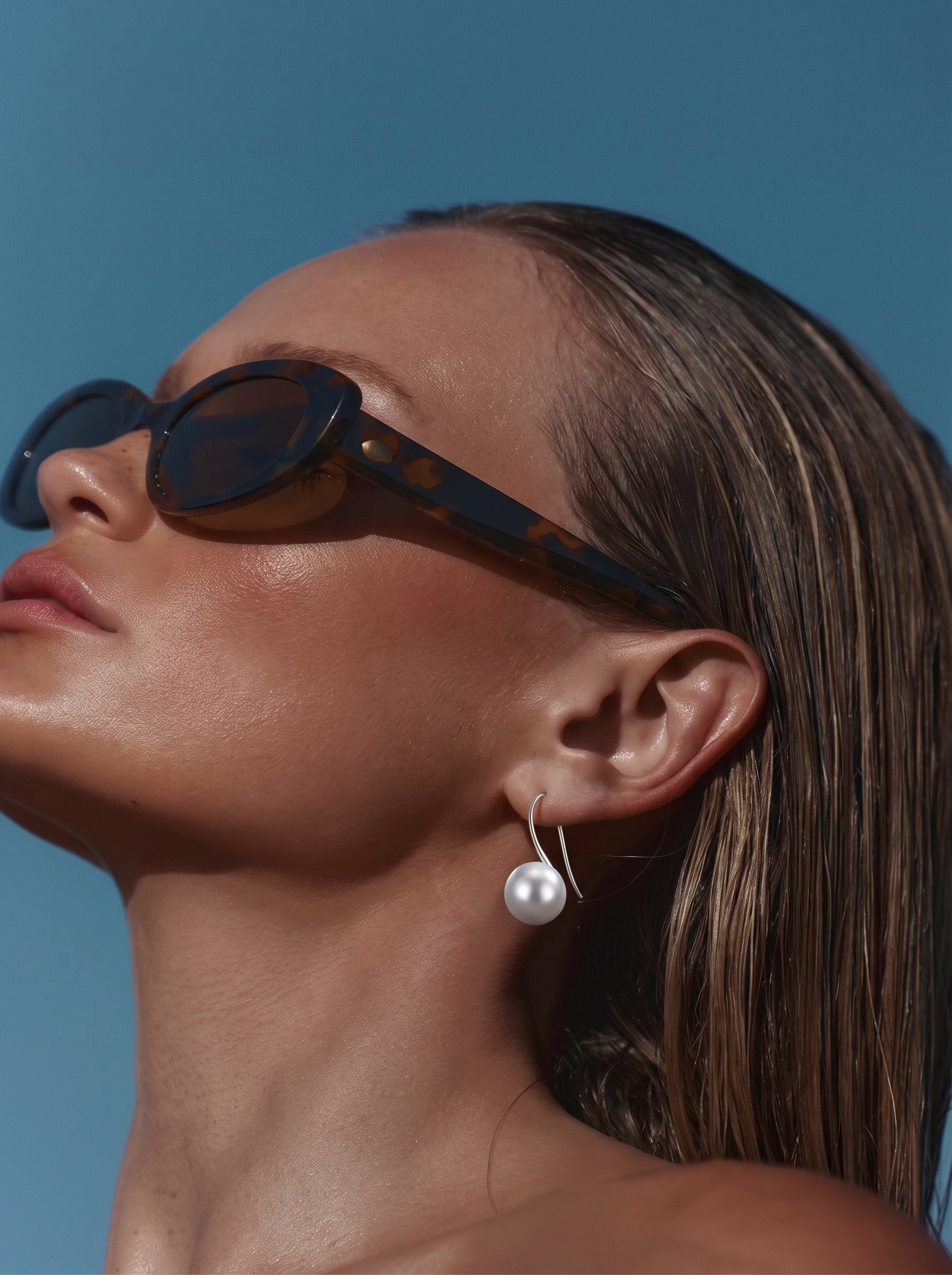 A woman wearing Alight Akoya Pearl Hoop Earrings and sunglasses against a blue sky. @lifestyle