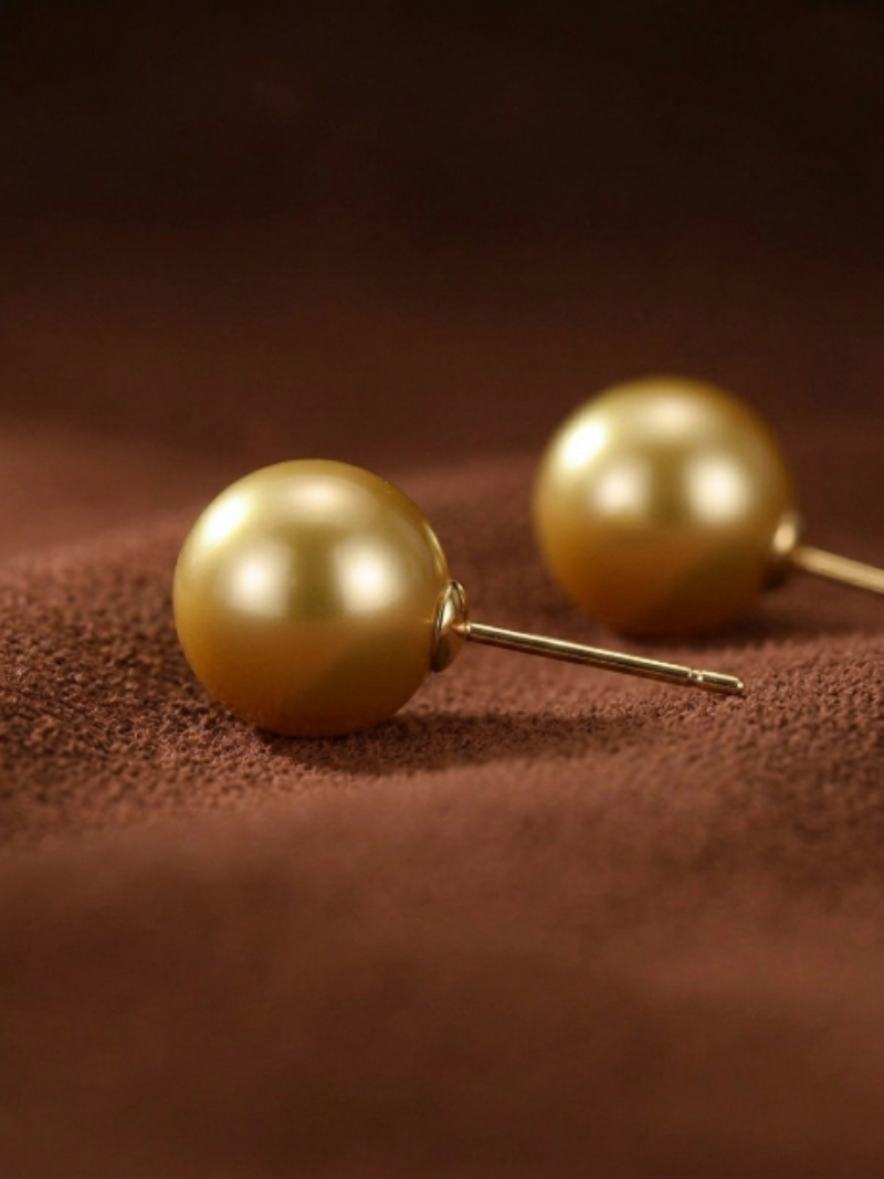 Close-up of two lustrous golden freshwater pearl stud earrings on a textured brown background.