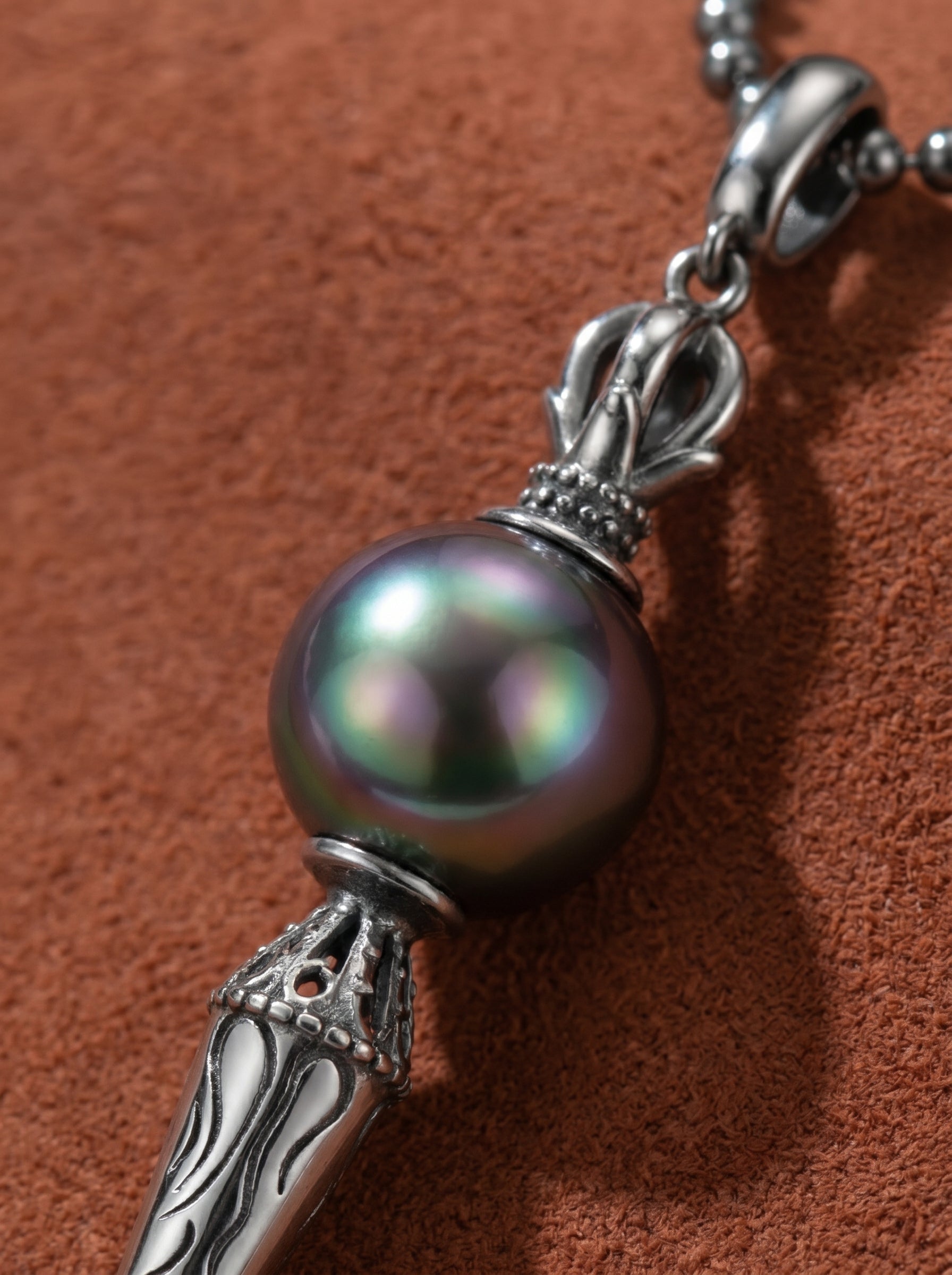 Close-up of a large drop necklace featuring a lustrous 10mm round Tahitian pearl with iridescent overtones, suspended from a silver ball chain and a detailed Phurba pendant. @pearl