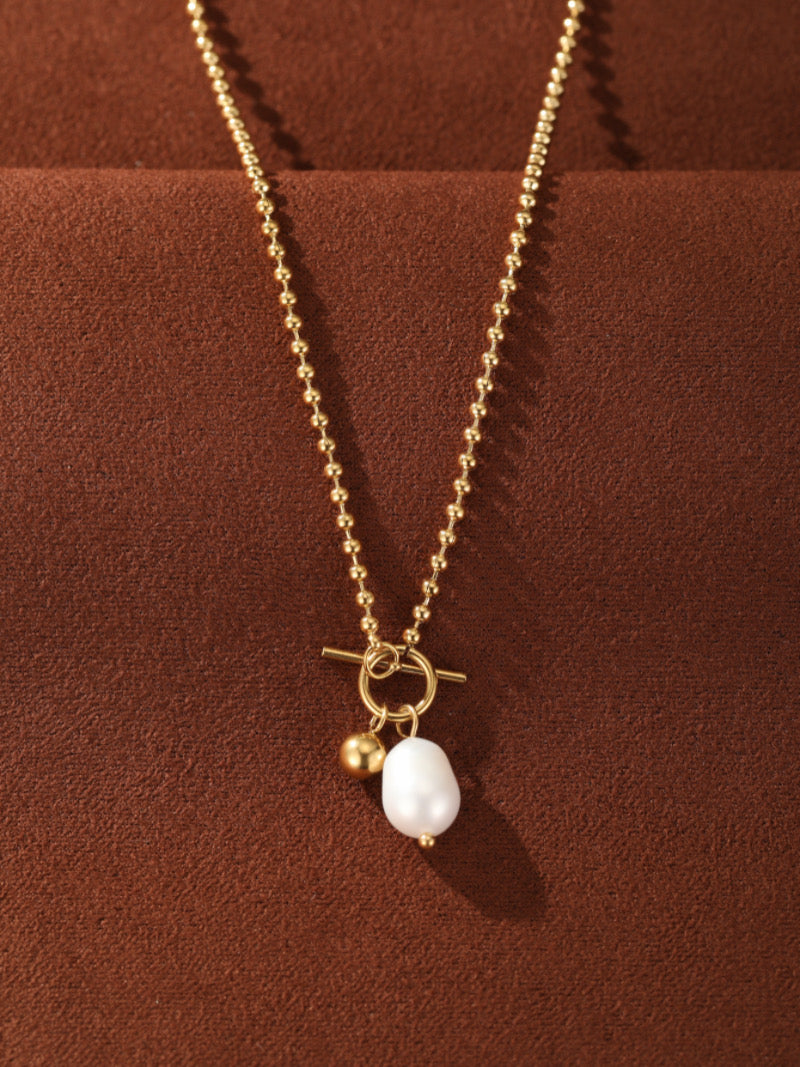 Gold-toned ball chain necklace with a chunky pendant featuring a white drop freshwater pearl and a small gold bead, fastened with a toggle clasp.