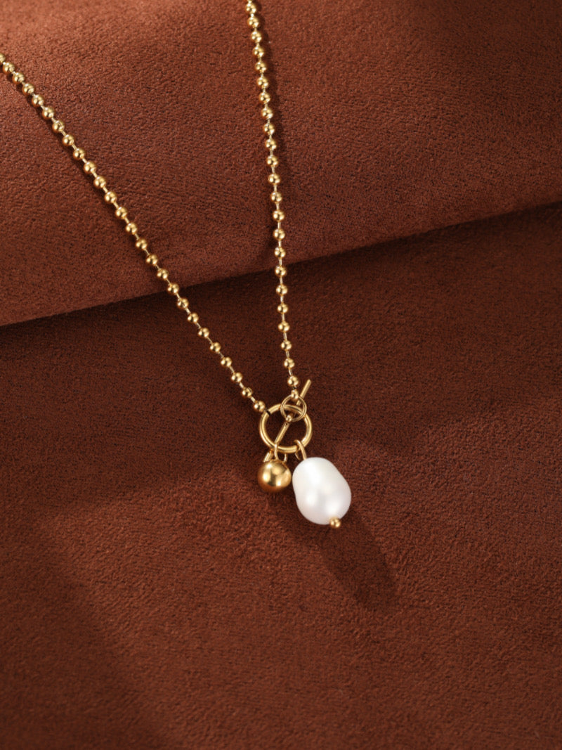 Gold-toned ball chain necklace with a chunky pendant featuring a white drop freshwater pearl and a small gold bead, fastened with a toggle clasp.