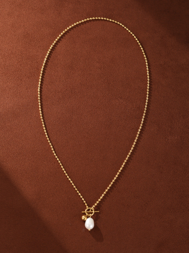 Gold-toned ball chain necklace featuring a chunky pendant with a white drop freshwater pearl and a toggle clasp.