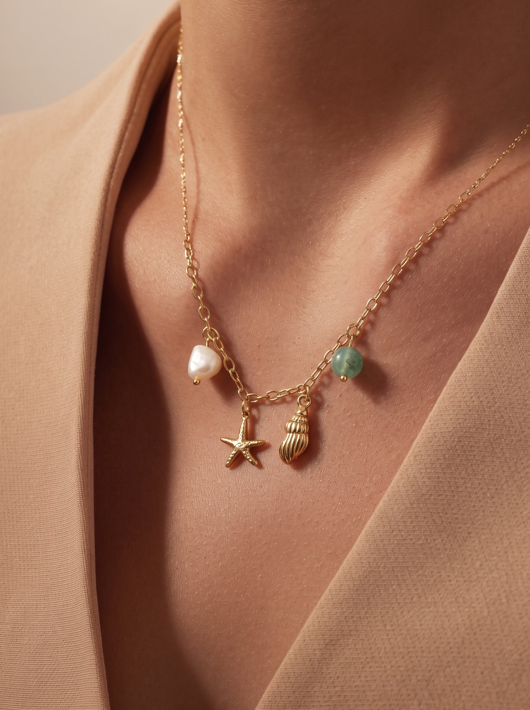 Collier doré avec une perle d'eau douce, une breloque étoile de mer, une breloque coquillage, et une perle verte, porté par une mannequin. @model